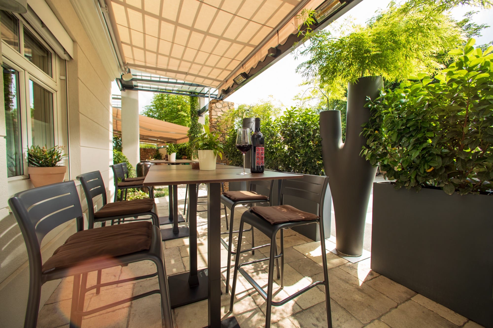 Die Terrasse unter der Markise, Stehtische zwischen Pflanzkübeln